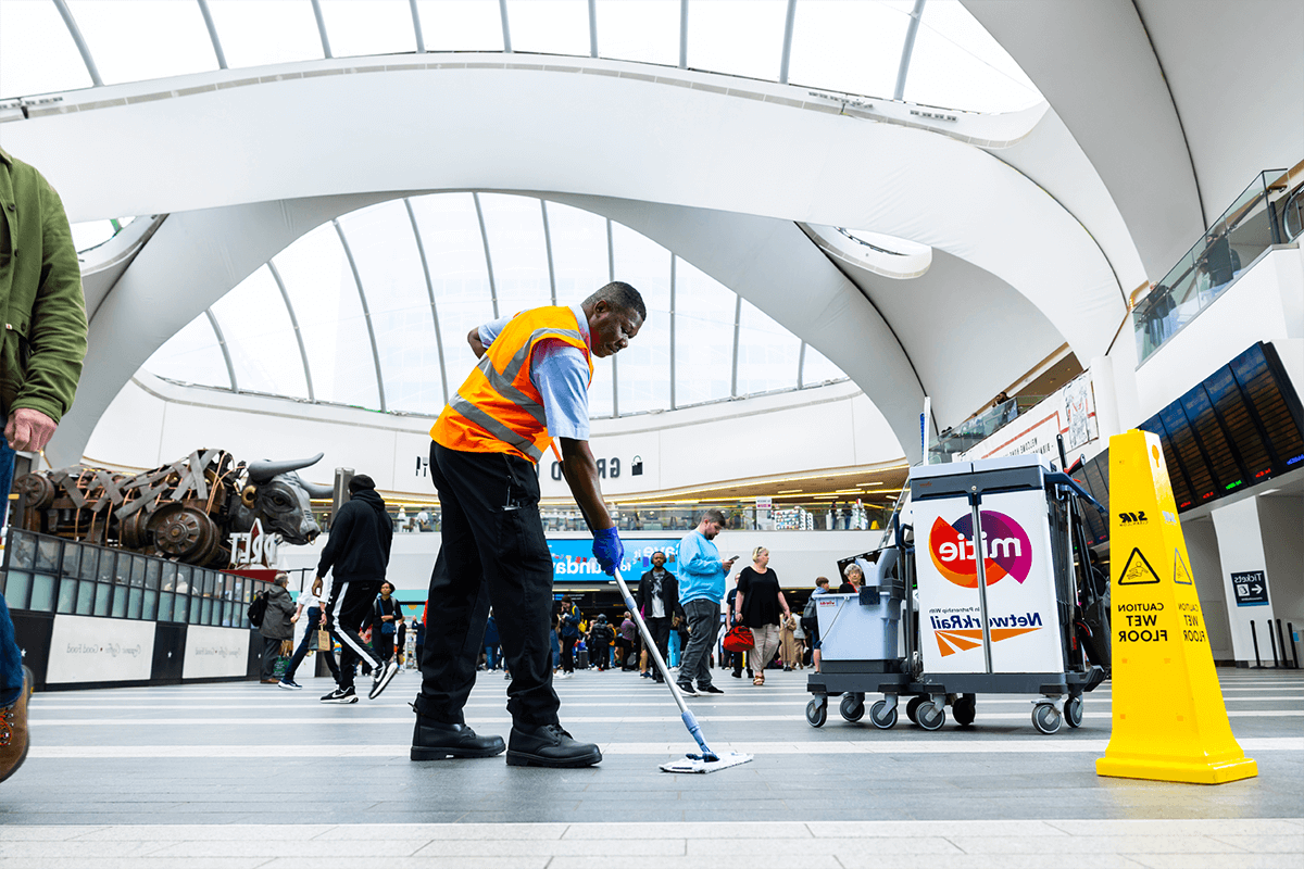 Mitie cleaner sweeping a floor in a busy railway station